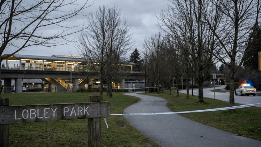 A wide-angle landscape photograph of Lobley Park in Burnaby at dusk, showing police tape blocking a path, a police vehicle with flashing lights, a "POLICE WARNING: STAY VIGILANT" sign, and a SkyTrain station in the background under an overcast sky.